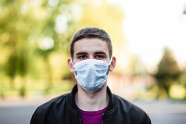 Koruyucu bir maske takan, şehirde yürüyen olgun bir adamın portresi. Mikropları, zehirli dumanları ve tozu önlemek için maske takan genç bir adamın görüntüsü. Bakteriyel enfeksiyonun önlenmesi - 19