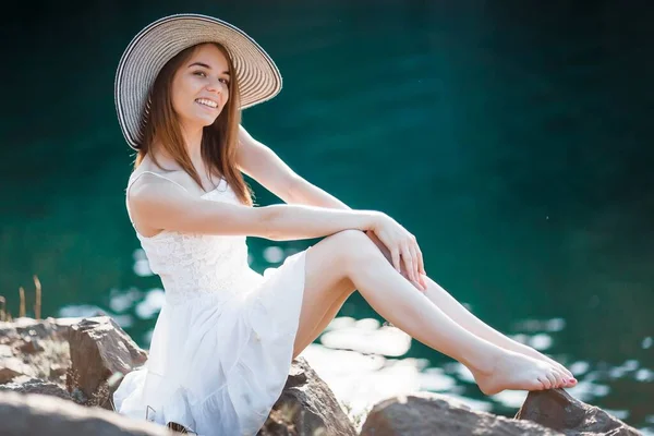 穿着白衣戴帽子的快乐的小女孩坐在石头上 在海边享受夏日 — 图库照片