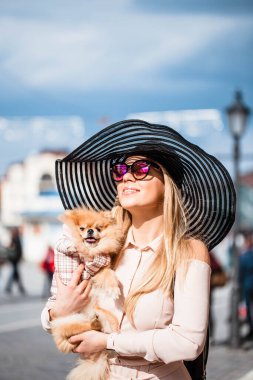 Beyaz pomeranya köpeğini elinde tutan pembe tişört ve aksesuar giyen çekici bir kızın portresi. Şirin Pomeranya tükürüğü. Köpekler ve insanlar arasındaki arkadaşlık..