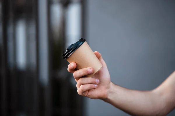 The guy holds a paper cup with coffee or tea. Have a cup of coffee. Disposable paper cup. Beautiful girl with blond hair. Casual style, white shirt and jeans. Take it away. Hot drink. Empty space.