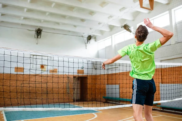 The guy jumped up to hit the volleyball ball. The guy plays volleyball in the gym. Volleyball. Ball. Volleyball net.