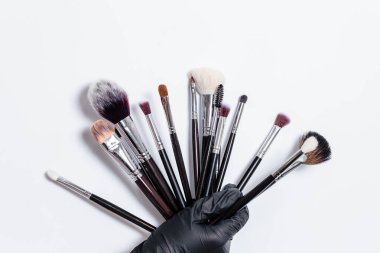 Profesyonel makyaj fırçaları beyaz arka planda izole edilmiş. Siyah bir eldiven, beyaz bir arka planda kozmetik için profesyonel fırçalar bulundurur. Uzayı metin için kopyala. Makyaj. Fırçalar.