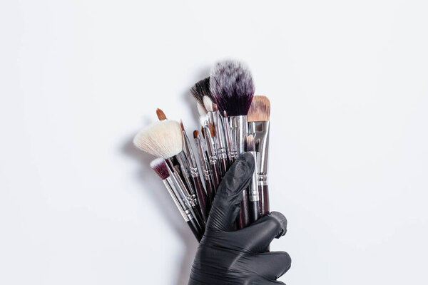 Professional makeup brushes isolated on white background. Hand in a black glove holds a set of professional brushes for cosmetics on a white background. Copy space for text. Makeup. Brushes.