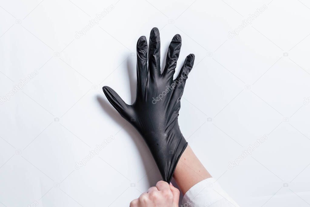 Hand in black gloves of a doctor or hairdresser on a white background. Gloves are worn on the hand. The girl puts a black glove on her hand. Black mitten on his hand.