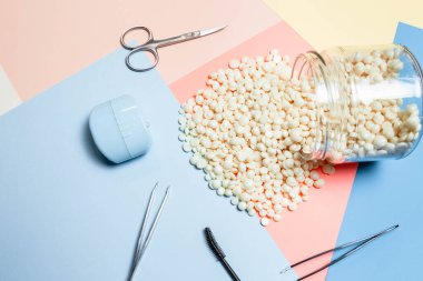 Beyaz inci rengi tüy dökülmesi için balmumu ve tahta sopa spatulası, su şişeleri, kaş jeli, cımbız, ruj, makyaj, pembe ve mavi ve beyaz arkaplan aynası..