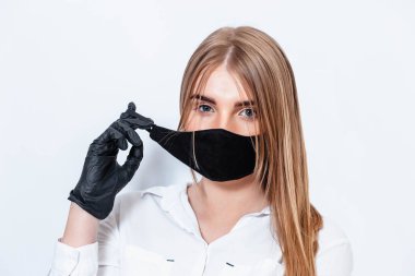 Beyaz takım elbiseli ve tıbbi maskeli bir doktor siyah eldivenlerle el ele tutuşup koronavirüs salgınının sonuçlarını düşünüyor. Beyaz arka planda bir doktor. Doktor siyah bir maske takıyor..