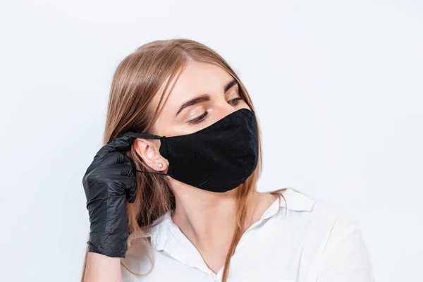 Beyaz takım elbiseli ve tıbbi maskeli bir doktor siyah eldivenlerle el ele tutuşup koronavirüs salgınının sonuçlarını düşünüyor. Beyaz arka planda bir doktor. Doktor siyah bir maske takıyor..