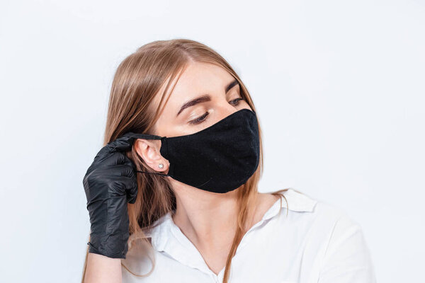 Doctor in a white suit and medical mask, holding hands in black gloves and thinking about the consequences of the coronavirus epidemic. Doctor on a white background. The doctor puts on a black mask.