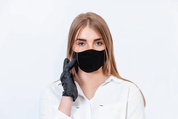 Beyaz takım elbiseli ve tıbbi maskeli bir doktor siyah eldivenlerle el ele tutuşup koronavirüs salgınının sonuçlarını düşünüyor. Beyaz arka planda bir doktor. Doktor siyah bir maske takıyor..