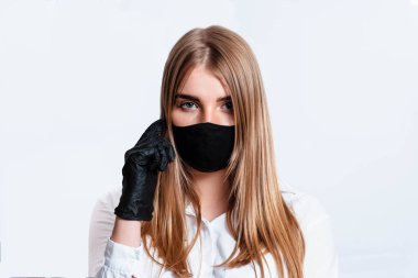 Beyaz takım elbiseli ve tıbbi maskeli bir doktor siyah eldivenlerle el ele tutuşup koronavirüs salgınının sonuçlarını düşünüyor. Beyaz arka planda bir doktor. Doktor siyah bir maske takıyor..