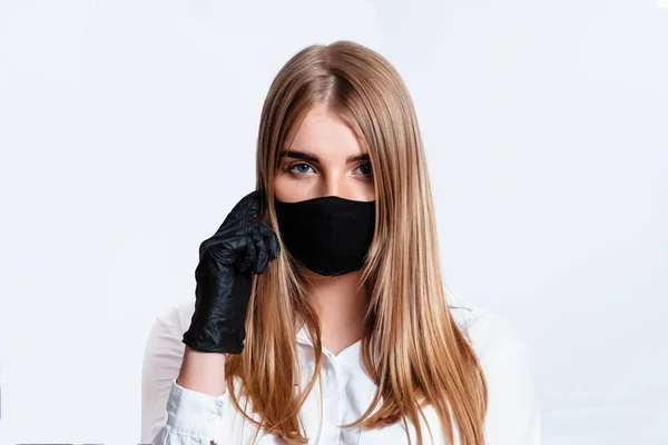 Beyaz takım elbiseli ve tıbbi maskeli bir doktor siyah eldivenlerle el ele tutuşup koronavirüs salgınının sonuçlarını düşünüyor. Beyaz arka planda bir doktor. Doktor siyah bir maske takıyor..