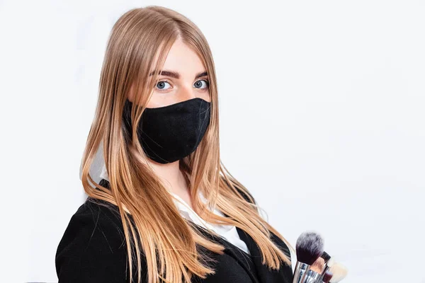 Beautiful young woman doing makeup. Girl with a brush in hand to apply powder on the face. Woman in black gloves makes makeup. Woman makes makeup herself on a white background.