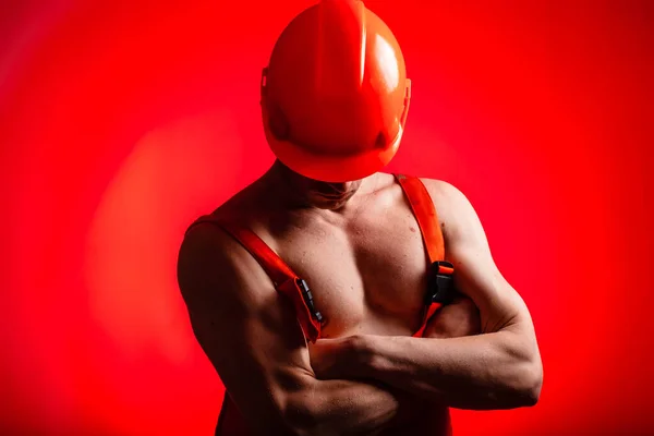 Kırmızı arka planda seksi bir müteahhit. Kafasında kask olan bir mimar. Seksi inşaatçı. Pompalı kollar ve sırt.