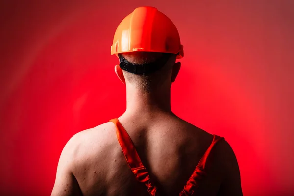 Sexy builder on a red background. Builder with a helmet on his head. Sexy builder. Pumped arms and back.