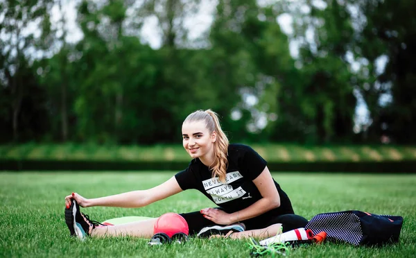 Healthy sports lifestyle. Athletic young woman in a sports dress doing fitness exercises. Fitness woman at the stadium. Young woman squats. The young girl goes in for sports. Fitness Sport. Stretching