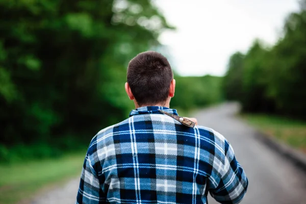 A lumberjack works in the forest. Lumberjack with an ax in the summer forest. The lumberjack is holding an ax. The lumberjack holds an ax on his back. The lumberjack shows the class. Ax in hand.