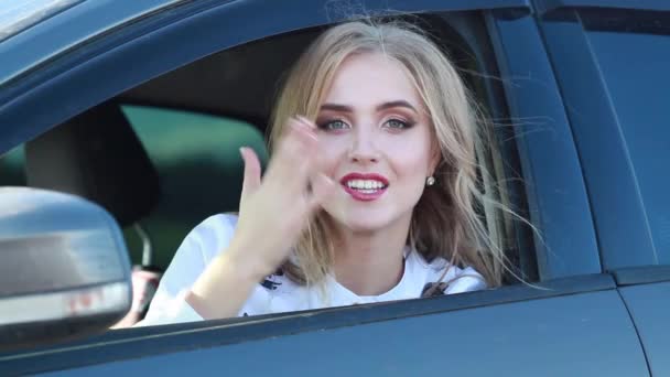 Beautiful blonde girl waving and sending kisses from the window of a car in summer — Stock video