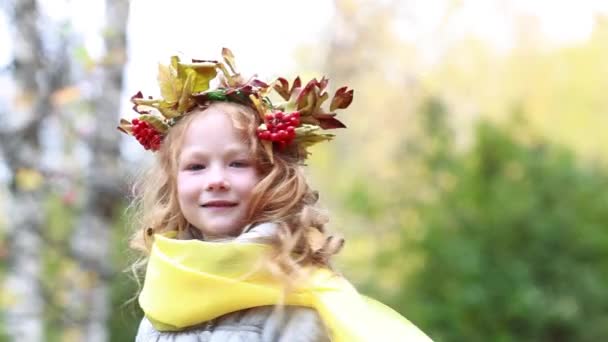 Mooi meisje 7-8 jaar met een krans van bladeren van de herfst voor mountain ash in het park op een zonnige dag — Stockvideo