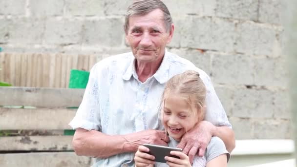 Abuelo y nieta jugando juegos en su teléfono móvil al aire libre día de verano — Vídeo de stock