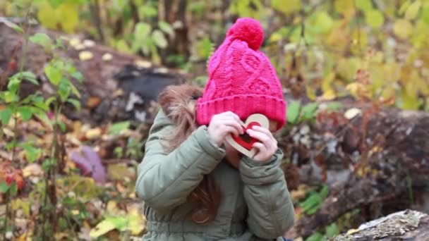 Chica con un corazón rojo en la naturaleza decorativa bosque de otoño — Vídeo de stock