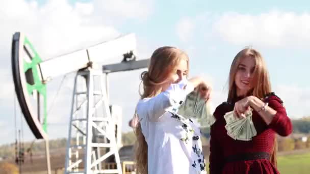 Two young rich girl happily throw dollars on the oil fields. Income from oil — Stock Video