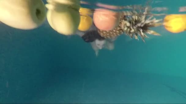 Schönes Mädchen schwimmt unter Wasser im Pool mit Früchten — Stockvideo