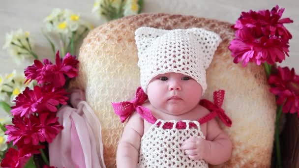 Bebé recién nacido en un sombrero blanco se encuentra en una cesta con flores rojas — Vídeo de stock