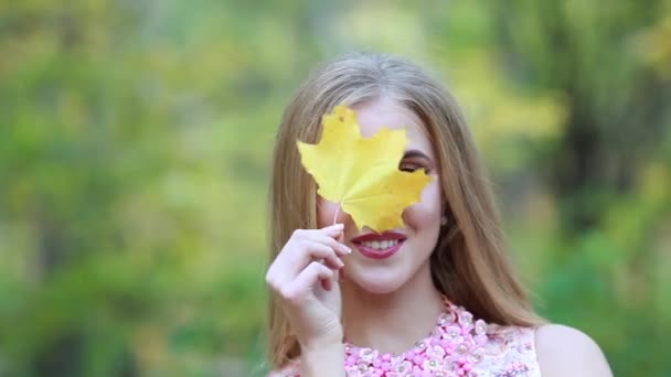 Uma menina na natureza com uma folha de bordo — Vídeo de Stock