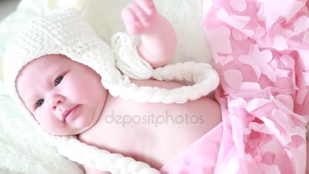 Um bebê em uma tampa de malha branca na cama olha para a câmera — Vídeo de Stock