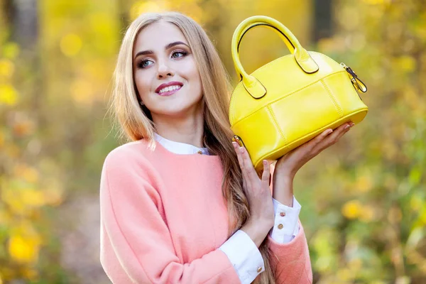 Mulher jovem bonita com bolsa na moda amarela em mãos na natureza de outono — Fotografia de Stock