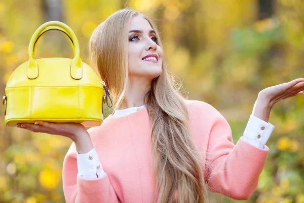 Mulher jovem bonita com bolsa na moda amarela em mãos na natureza de outono — Fotografia de Stock