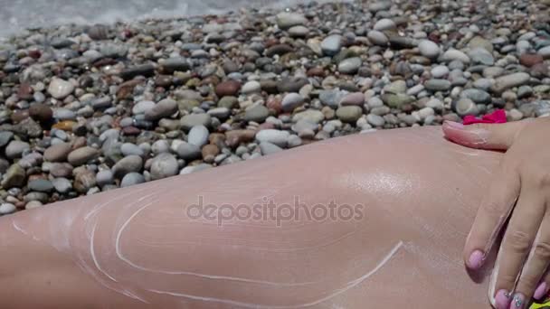Ein junges Mädchen schmiert sich am Strand mit der Hand Sonnencreme an die Füße. 4 k