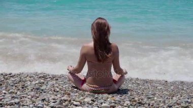 Güzel genç kız onu geri bir lotus poz ile sahilde oturuyor. 4k