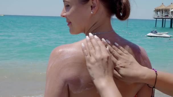 Дівчина застосовує сонцезахисний крем на пляжі.4k — стокове відео