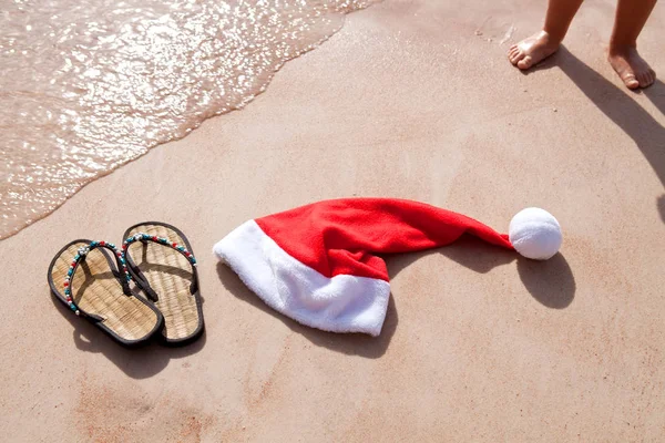 Czerwony kapelusz santa i klapki na żółty piasek na plaży — Zdjęcie stockowe