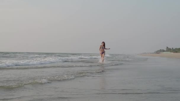 El traje de baño femenino corre a lo largo de la orilla del Océano Índico hacia adelante, mirando a la cámara. 4K — Vídeos de Stock