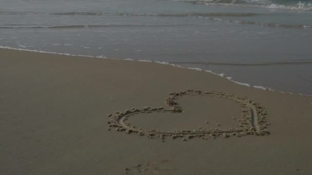 Сердце на песке пляжа с волной на заднем плане. 4K — стоковое видео