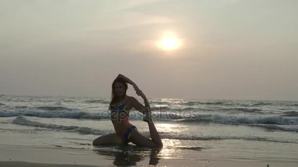 Красива струнка дівчина в купальнику займається йогою на пляжі на заході сонця. 4-кілометровий — стокове відео