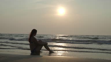 Kız günbatımında beach rüya üzerinde oturuyor. 4k