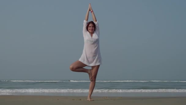 Mujer joven que practica yoga en los árboles posa cerca del océano. 4K — Vídeo de stock