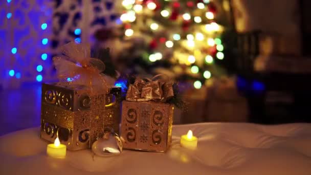 Две золотые резные коробки с луком и свечами на фоне горящих гирлянд в новогоднем интерьере — стоковое видео