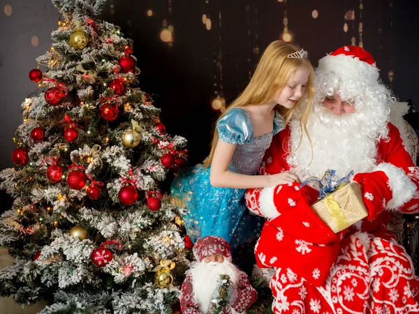 Noel Baba ve Noel ağacının yanında küçük bir kız içeride bir hediyeyi inceliyor. — Stok fotoğraf