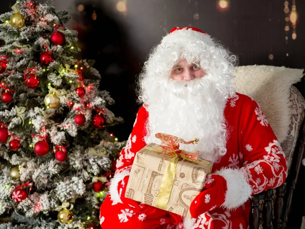 Santa Claus con un regalo se sienta junto al árbol de Año Nuevo — Foto de Stock