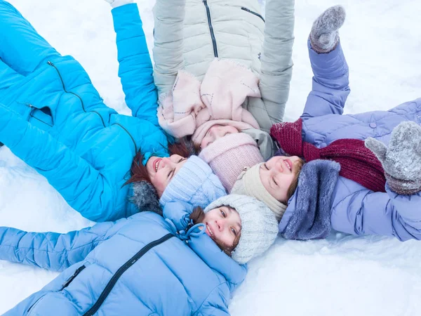 Красивые веселые девушки в шляпах и зимних куртках лежат на снегу улыбаясь — стоковое фото
