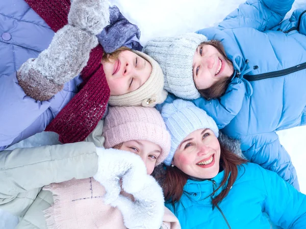 Четыре красивые улыбающиеся девушки лежат лицом к лицу в снегу, смотря в камеру. — стоковое фото