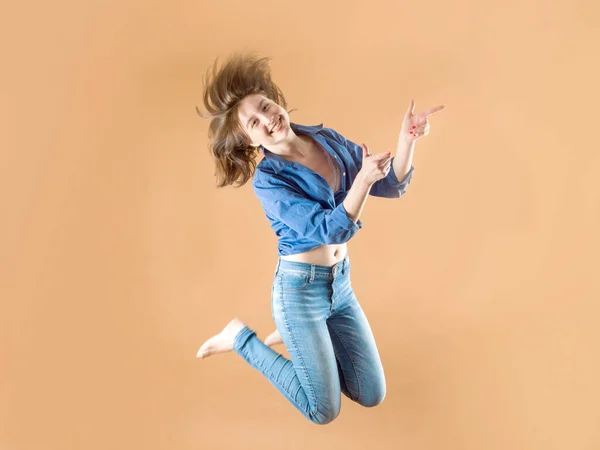 Mooi meisje in jeans in een sprong geeft de richting van de vinger op een bruine achtergrond — Stockfoto