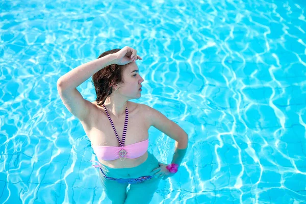 Menina bonita nova em um maiô rosa posando em uma piscina com água azul. Resort de viagem — Fotografia de Stock