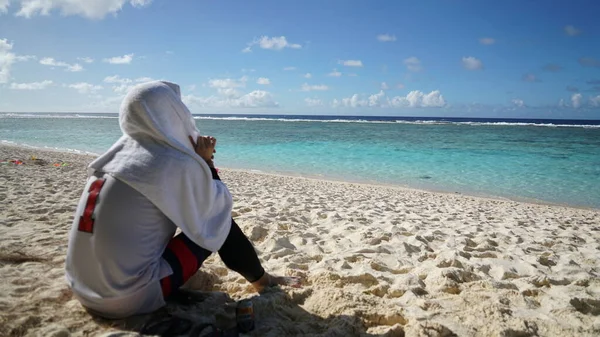 Kafasının üstünde havluyla derin düşünen bir adam mavi denize bakıyor..
