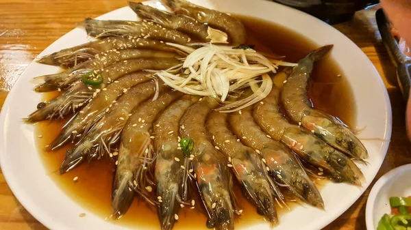 Beyaz tabak üzerine kırmızı biber ve maydanoz serpiştirilmiş tereyağlı sarımsaklı karides, küçük kasede soya sosu, ahşap masa, yukarıdan görüş.