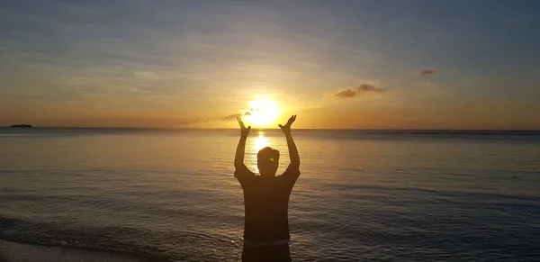 Kendine güveni tam bir adam. Gün doğarken deniz kenarında kollarını açıyor.